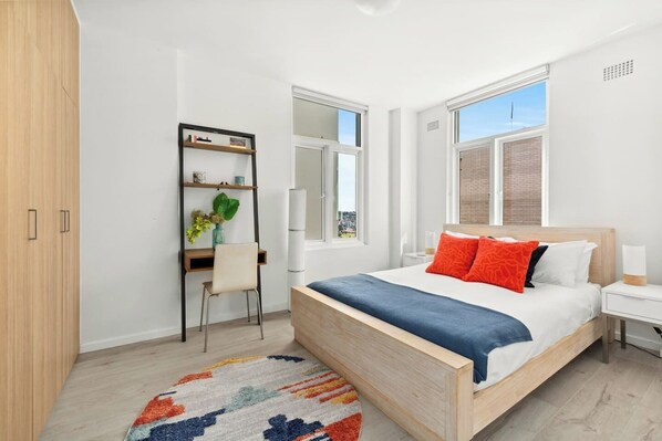 The spacious, light-filled first bedroom features a queen-size bed, while a desk provides a space to work or study.
