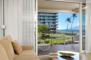 Soft sand-toned seating and sheer drapes frame the lush palms and ocean glimpses beyond the private lanai     WH1-211