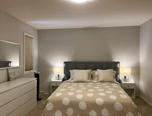 Large ensuite primary bedroom with queen size quilted bed and lots of storage.