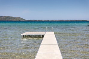 A wooden dock juts out into the calm lake. The water reflects the clear blue sky