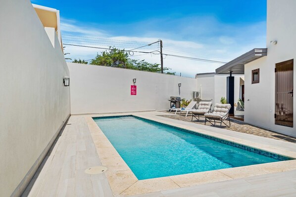 The backyard features a sleek, pool with crystal-clear water, perfect for relaxing or swimming laps - Lounge chairs and a barbecue area provide a perfect setting for outdoor gatherings - Enclosed by walls, the area ensures privacy and tranquility