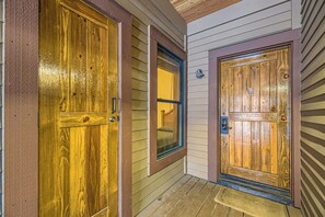 A narrow porch features two closed wooden doors—one on the left and one straight ahead—each framed with brown trim. A small lit window is situated between the doors. The floor is wooden planks.