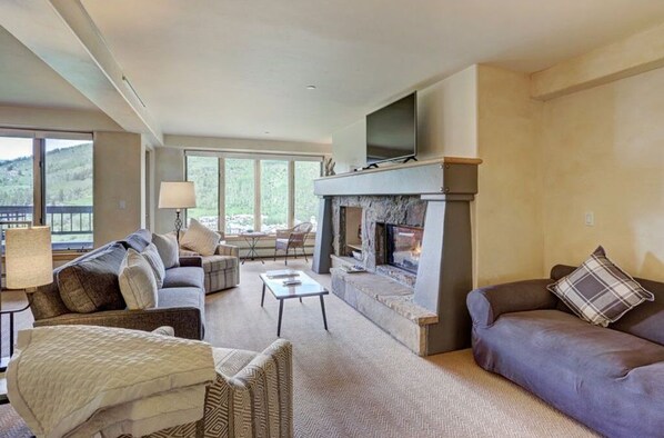 Enjoy the cozy living room featuring a comfortable seating area, a charming fireplace, and large windows that fill the space with natural light.