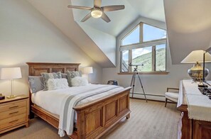 Relax in the spacious bedroom with a vaulted ceiling, a plush king-sized bed, and large windows offering picturesque views.