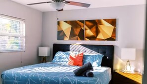 Discover tranquility in Bedroom 1, where a plush bed takes center stage, flanked by elegant side tables. The walls adorned with captivating paintings frame the space, while the gentle breeze of the ceiling fan complements the view through the windows