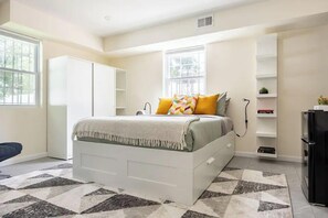 Spacious studio with cozy queen bed, smart TV, stylish shelving, and bright elegant decor.