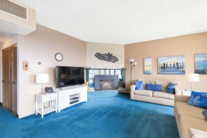 Open and inviting living room featuring a cozy fireplace and plenty of seating wrapped by large windows allowing natural light to enter.