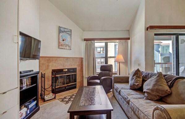 Relax in the spacious living room featuring a large flat-screen TV, comfortable seating, and plenty of natural light from the windows.