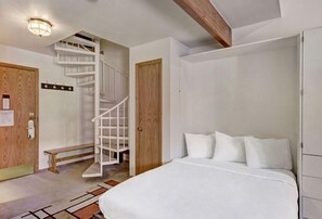 Retreat to the charming loft bedroom, accessible via a unique spiral staircase, featuring a comfy bed and a rustic wooden beam ceiling.