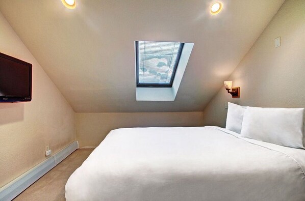 Sleep soundly in the cozy attic bedroom featuring a queen-sized bed, skylight, and modern lighting for a serene atmosphere.