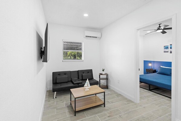 Our living room features a small sofa, a television, a table, and air conditioning.