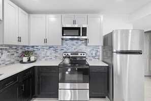 A stove with 4 Burner, a refrigerator, kitchen utensils including pots, pans, glasses, cutlery, and plates to cover all your needs, a sink, cabinets with ample space, a round table, and two chairs.