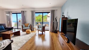 Discover Mon Rêve Portugais in Funchal, Madeira: A traditional two-story house featuring a spacious living room with a big smart TV, and a stunning terrace with sun loungers and a dining table.