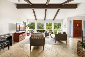 Living room with a nature view, a smart TV, and an upright digital piano.