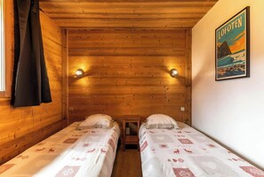 This cozy bedroom features two single beds with a festive patterned duvet, perfect for a relaxing night's sleep after a day on the slopes. The room is beautifully decorated with wood paneling and warm lighting, creating a warm and inviting ambiance.