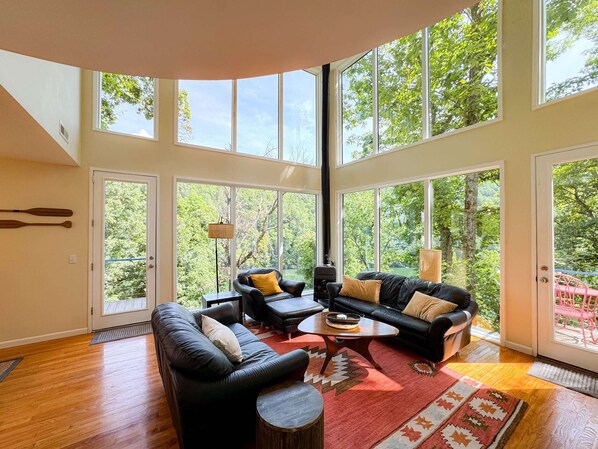 Spacious living room with a stunning mostly glass exterior wall. Unwind from a day of outdoor adventure and exploring hanging out in the trees!