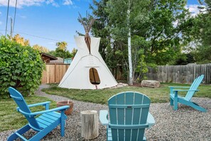 An inviting outdoor experience including an authentic canvas tepee, grapevine covered swing, and a firepit stove.