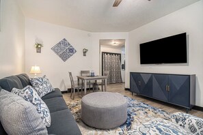 Living Rm with Fan, Couch, Table for 2 and a Smart TV.