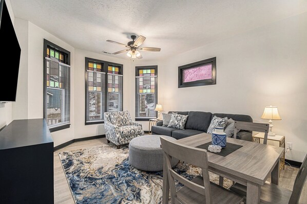 Living Rm with Fan, Couch, Table for 2 and a Smart TV.