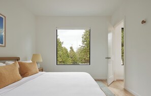 A bedroom with an inviting bed and a large window, bringing the forest views inside.