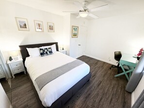 Relax in this bright, spacious bedroom featuring a plush queen bed, work desk, ceiling fan, and clean modern design.