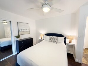 Comfortable queen-size bed, dresser storage, and ceiling fan in a calming, light-filled space.
