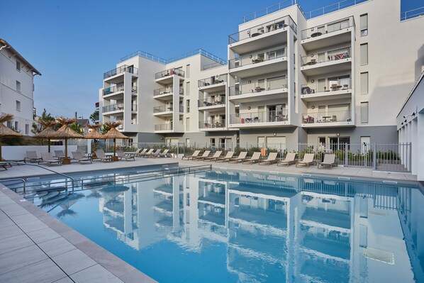 Relax by the stunning outdoor pool, surrounded by modern apartment buildings and plenty of lounge chairs for sunbathing. Perfect for a refreshing dip or enjoying a sunny afternoon.