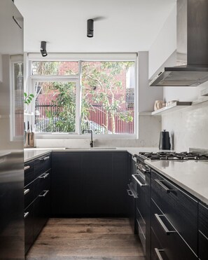 This sunlit, modern kitchen is fully equipped with quality appliances, stone benchtops, and stylish black cabinetry — perfect for preparing meals in style