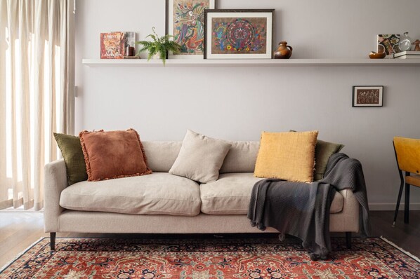 Relax in the inviting living room, styled with a plush neutral sofa, vibrant cushions, a vintage rug, and curated artwork for a warm, homely feel