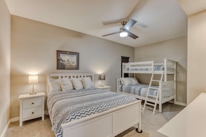 Family-friendly room with a queen bed, bunk beds, closet, nightstand, and warm lighting—blending comfort, function, and minimalist style.