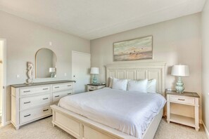 Unwind in style! This serene bedroom boasts a comfortable white bed, ample storage with a chic dresser, and soothing lighting for a restful stay.