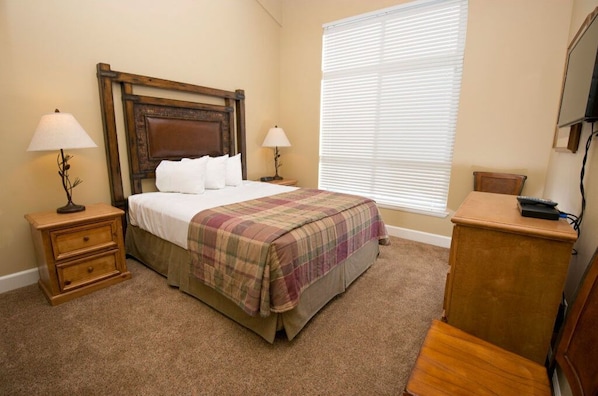 This bright bedroom features a comfortable queen bed, stylish rustic decor, and large windows letting in plenty of natural light.