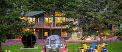 This stunning backyard features a glowing fire pit, a cozy heated igloo, and a barrel sauna, all set against a picturesque forest backdrop.