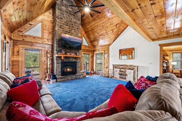 The spacious living room includes large windows, comfortable furniture, a smart TV, and a stone gas fireplace.