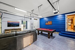 The newly renovated game room includes a large Smart TV, comfortable furniture, a pool table, arcade games, and more.