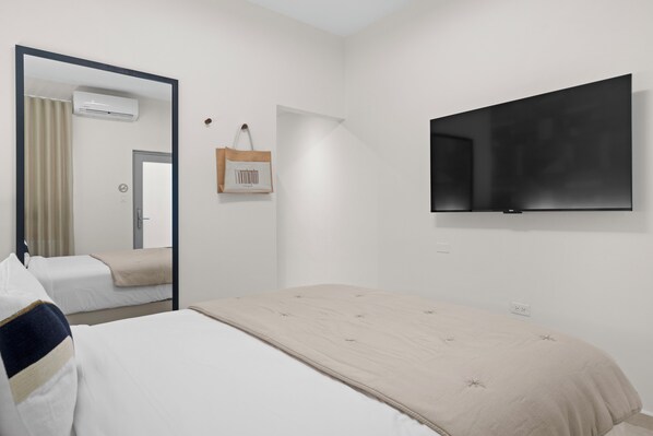 Spacious bedroom with a plush queen bed, a full-length mirror, and a flat-screen TV for ultimate relaxation.