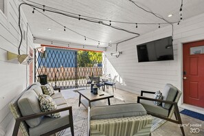 Covered patio with fenced-in yard comes with smart TV, outdoor dining area, lounge chairs, heaters, grill, and stream lights