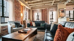 Cozy living room with exposed brick walls, plush seating, and ample natural light, creating a perfect space to relax and unwind.