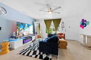 Living room with ceiling fan, large Tv with PS5 and fireplace