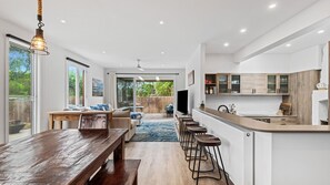 Open plan kitchen/ dining area with 4 stools at the breakfast bar and a large dining table wiht bench seats. 