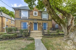 Enjoy a charming stay in this classic brick building with lush greenery and a welcoming front porch.