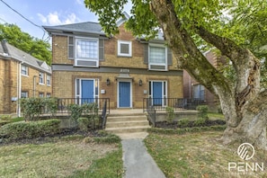 Enjoy a charming stay in this classic brick building with lush greenery and a welcoming front porch.