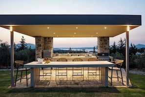 Οutdoor high-top dining area for 6 guests under a shaded pergola, adjacent to the BBQ.