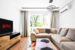 Unwind in this bright and inviting living room, where comfort meets modern design. Enjoy a cozy evening on the plush sofa, streaming your favorite shows on the smart TV, with a view of the lush greenery just outside the large windows.