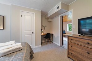 This bedroom features a queen bed, black out curtains, desk area and TV