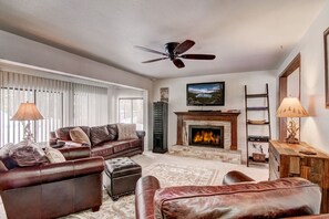 Cozy up by the fireplace in a spacious living room with natural light and mountain charm.