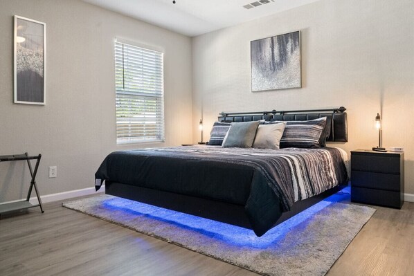Secondary bedroom at middle of house, with LED lighted floating King bed, Smart Fire TV, nightstands with USB and Plugs, ceiling fan, Dresser, and luggage rack