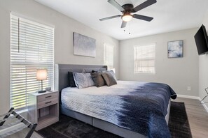 Primary bedroom at front of house, with King bed, en-suite bathroom, Smart Fire TV, nightstands with USB and Plugs, ceiling fan, and luggage rack