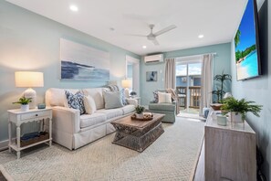 Airy, beachy living room with plush seating, natural light & balcony access.