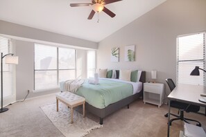 This bedroom is a serene retreat with cozy bedding, a calming color palette, and large windows offering a peaceful view and plenty of natural light, creating the perfect space for ultimate comfort and relaxation.